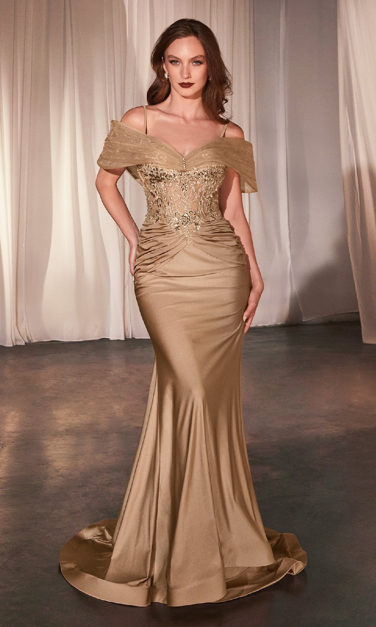 A woman wears the Sheer Lace-Bodice Long Prom Dress (CLCD798), featuring a gold, off-the-shoulder design with beaded embellishments, standing on a smooth floor with sheer curtains behind her.